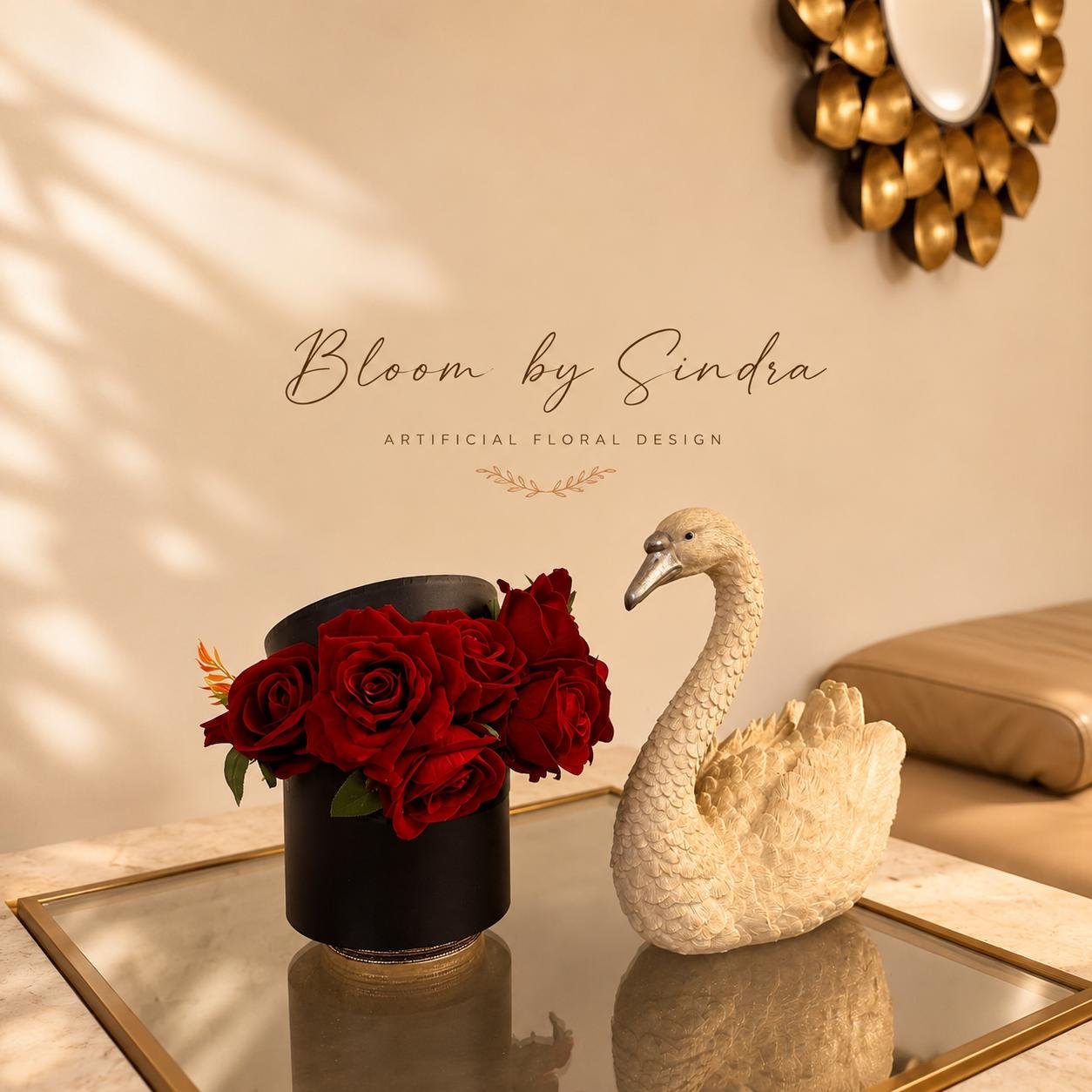 Bloom by Sindra branded photo of deep red roses in a black box vase beside a carved swan figurine